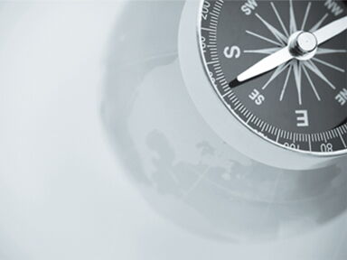 Teilansicht eines Kompasses vor grauem Hintergrund.