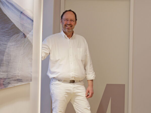 Dr. Schröder steht im Flur und blickt freundlich in die Kamera.