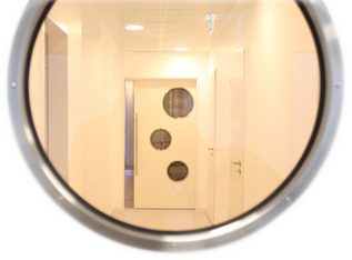 Blick durch ein rundes Fenster auf die Tür zum Operationssaal.